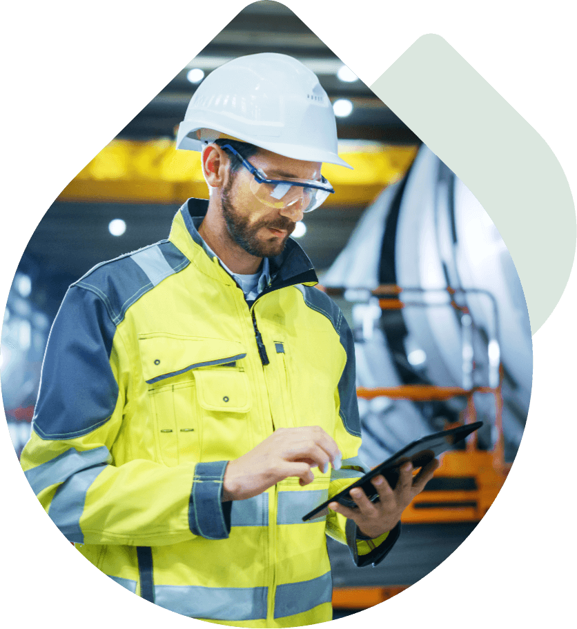 Industrial engineer in a high-visibility jacket and hard hat using a tablet in a modern factory or warehouse setting.
